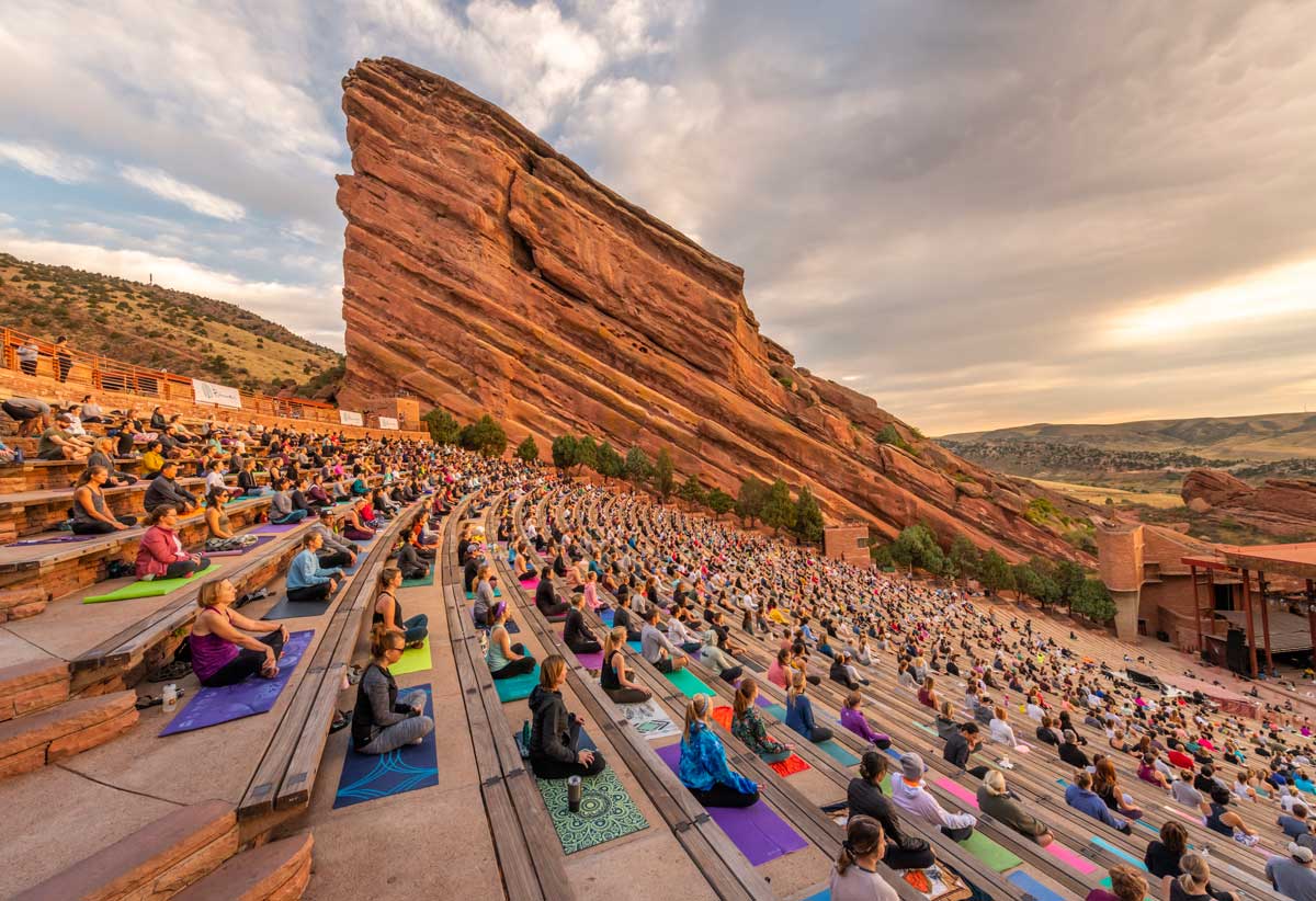 Large group of people perform yoga at an outdoor mountain venue during sunrise