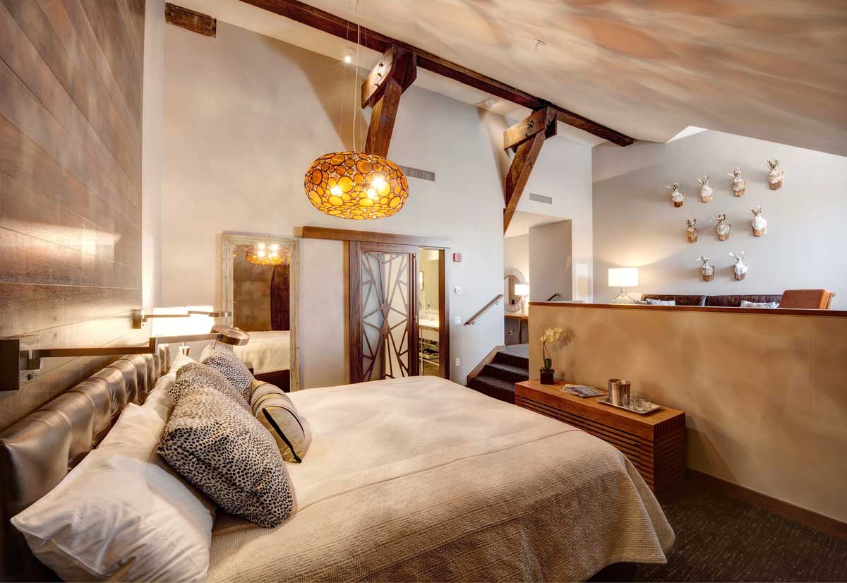 A cozy hotel room filled with earth tones, a huge bed with a lot of pillows on it and orange globe lighting