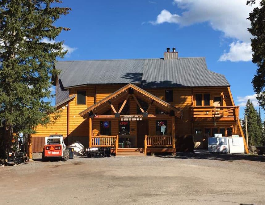 The Grand Mesa Lodge is made of golden-colored wood and offers a welcoming front porch with an open sign in the window.