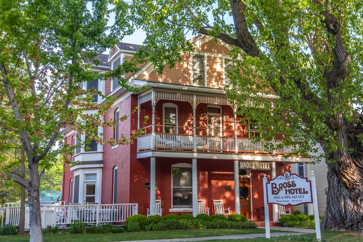 Bross Hotel Bed & Breakfast seen from the exterior with green, leafy trees all around; the three-story Victorian home is painted red with white trim.