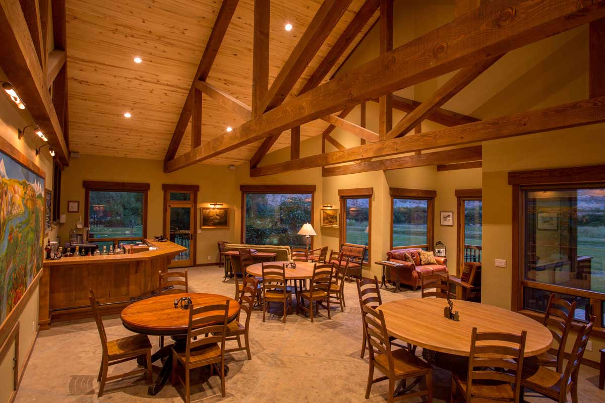 Gunnison River Farms dining-room interior with a high ceiling accentuated by beams, a bar and round wooden tables
