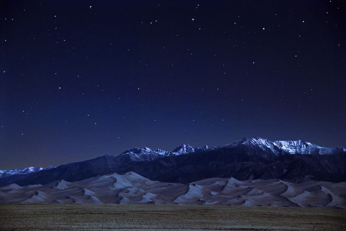 Night sky with stars above snowy mountains and sand dunes