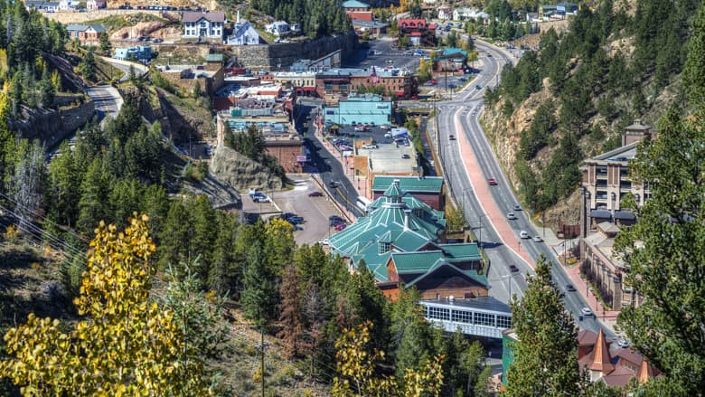 Black Hawk from above in the summer with evergreen trees, historic buildings and a road with a handful of cars driving by.
