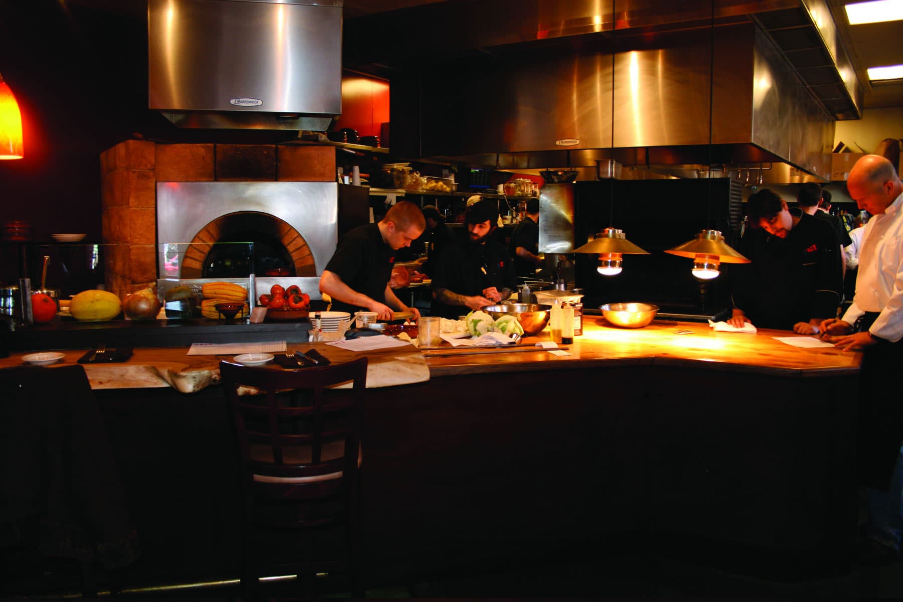 Chefs work in a kitchen beneath a brass hood