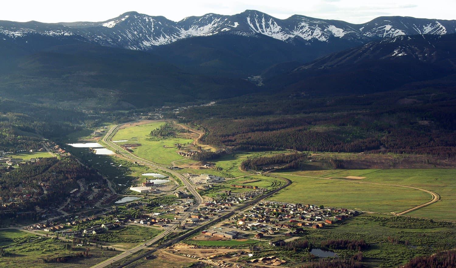 A summer aerial view of  Fraser with snow-dusted mountains in the background.