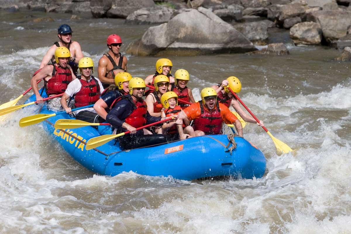 Eight people in red lifejackets inside a blue raft paddle through white rapids