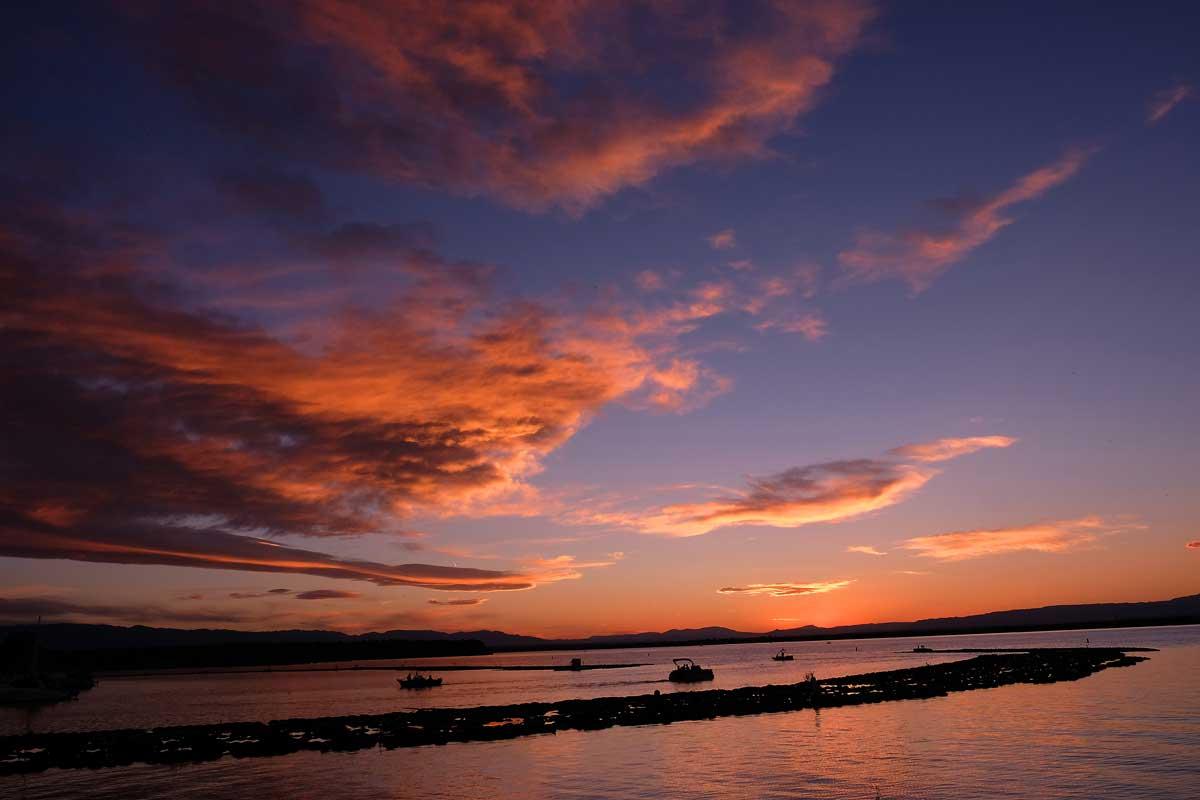 A setting sun paints the sky over Lake Pueblo State Park deep blue and vibrant orange-pink. Boats on the lake head towards shore.