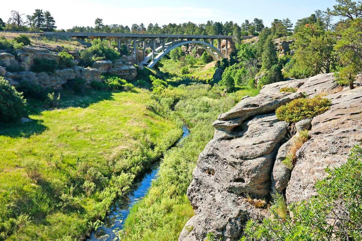 A narrow waterway weaves through a green meadow valley in Castlewood Canyon State Park.