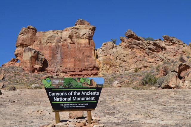 Canyons of the Ancients red-rock formations with sign that reads "Canyons of the Ancients National Monument" in foreground