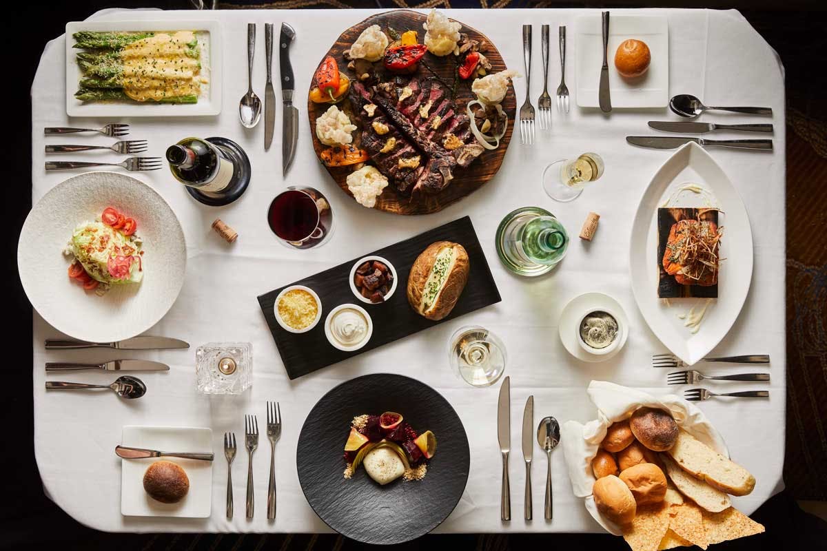 Plates line the a beautifully set table with steaks, potatoes, bread, asparagus and other fine foods at the Chop House at Monarch Casino