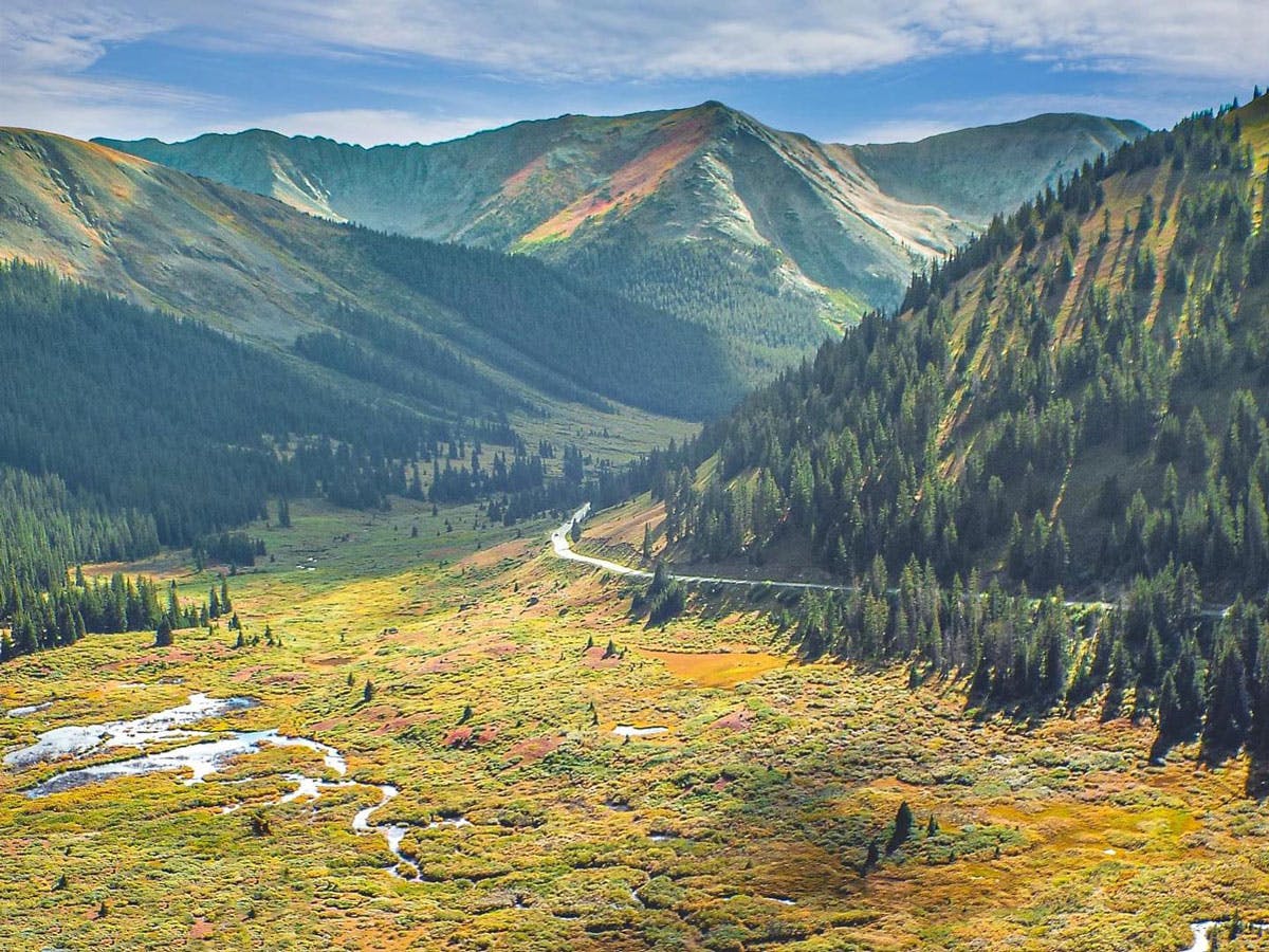 A meandering road cuts through sunlight-dappled mountain scenery near Leadville and Twin Lakes.