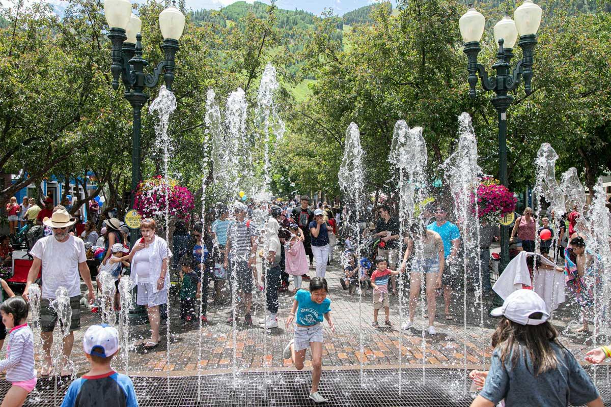 In town, a dancing water fountain shoots sprays of water. Kids play in it while adults watch on next to Aspen's old-timey street lamps