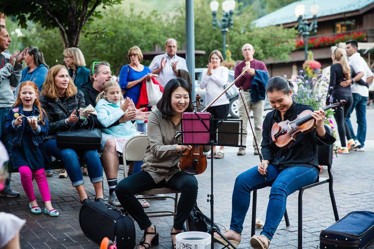 Two violinists entertaining a large group of people on the street in downtown Aspen.