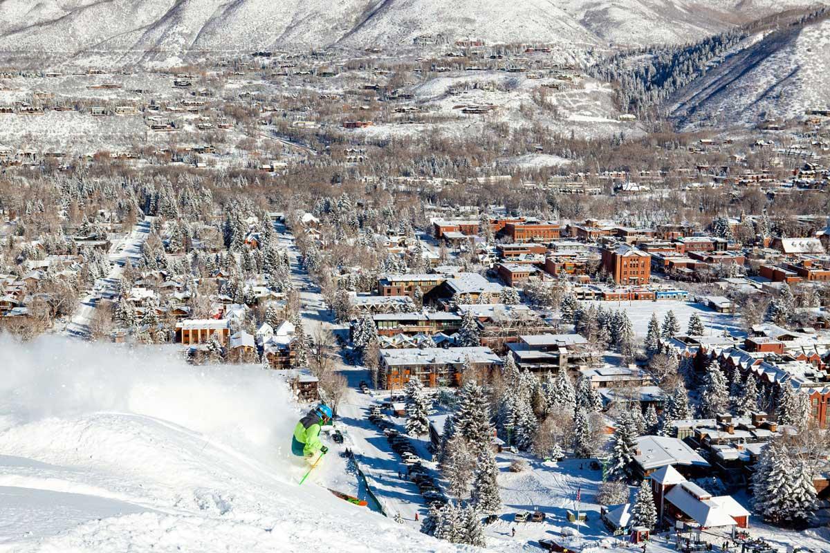 A skier, in neon green, rides down a mountain with a view of a snow-covered town in the background.