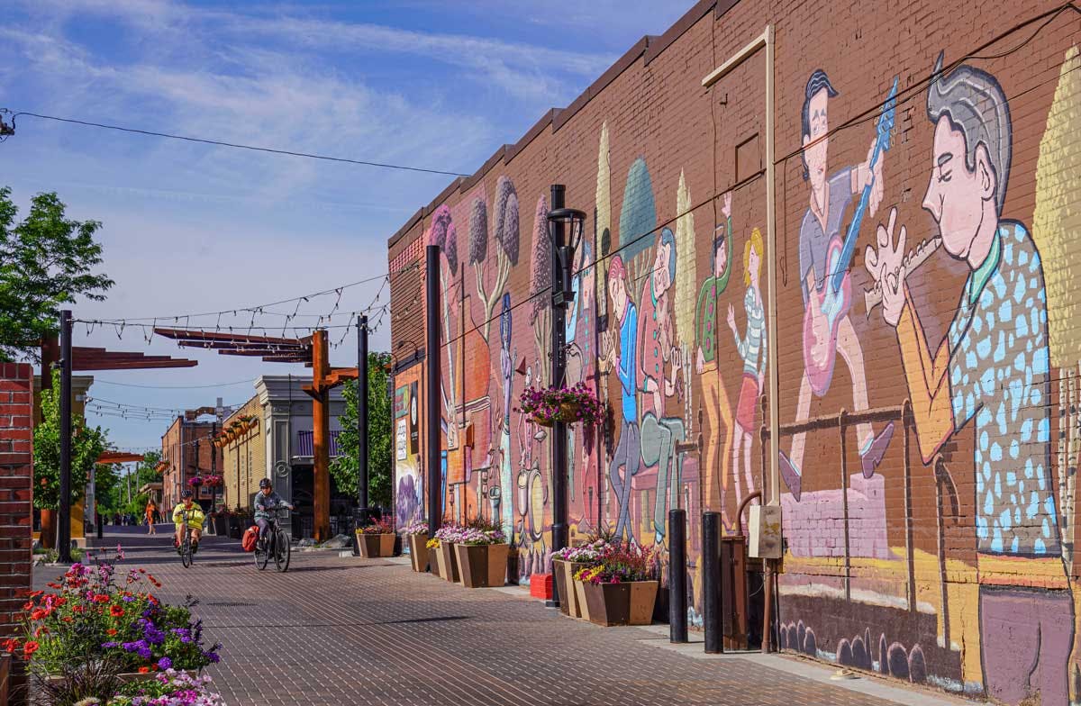 An alley in Fort Collins, Colorado, is set with many decorative geometrical planters filled with blooming flowers. The red-brick wall of a building is painted with a music-themed mural.