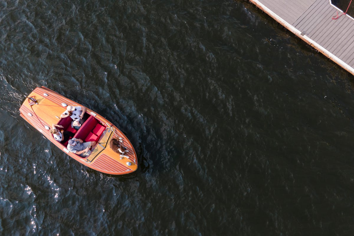 An aerial view of a wooden boat on Grand Lake's dark waters. A dock sits in the upper right corner.