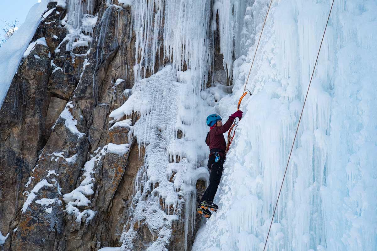 A climber in a maroon jacket and blue helmet scales the ice at the Lake City Ice Climbing Festival in Colorado.