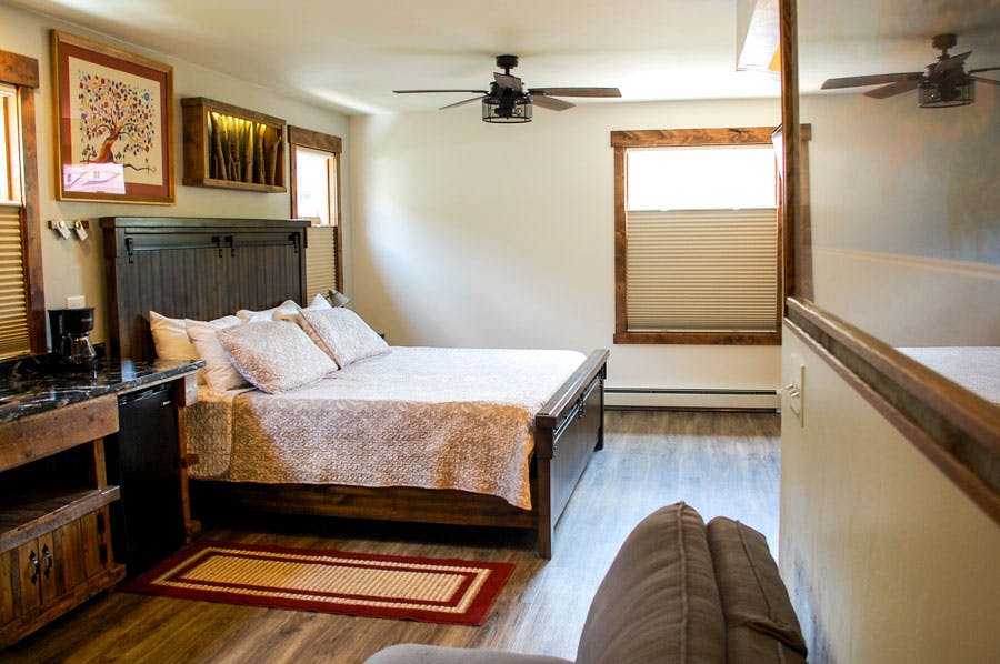 A cozy historical hotel room in Georgetown, Colorado with a ceiling fan, hardwood floors and a dark wooden bed frame.