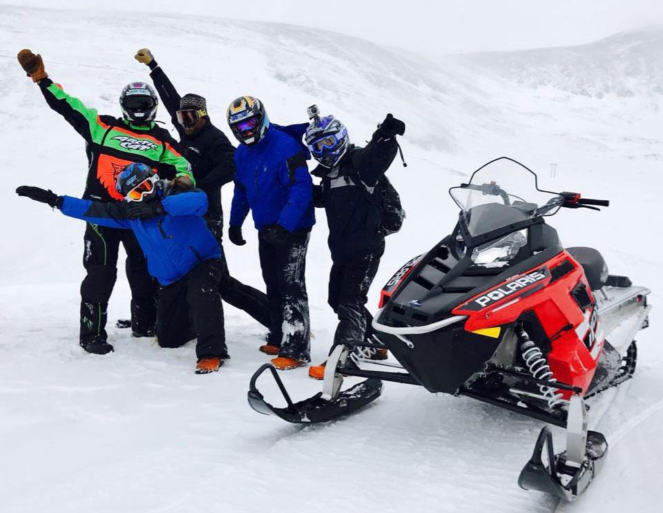 Snowmobilers with High Country Tours pause by their snowmobile with arms in the air near Kremmling