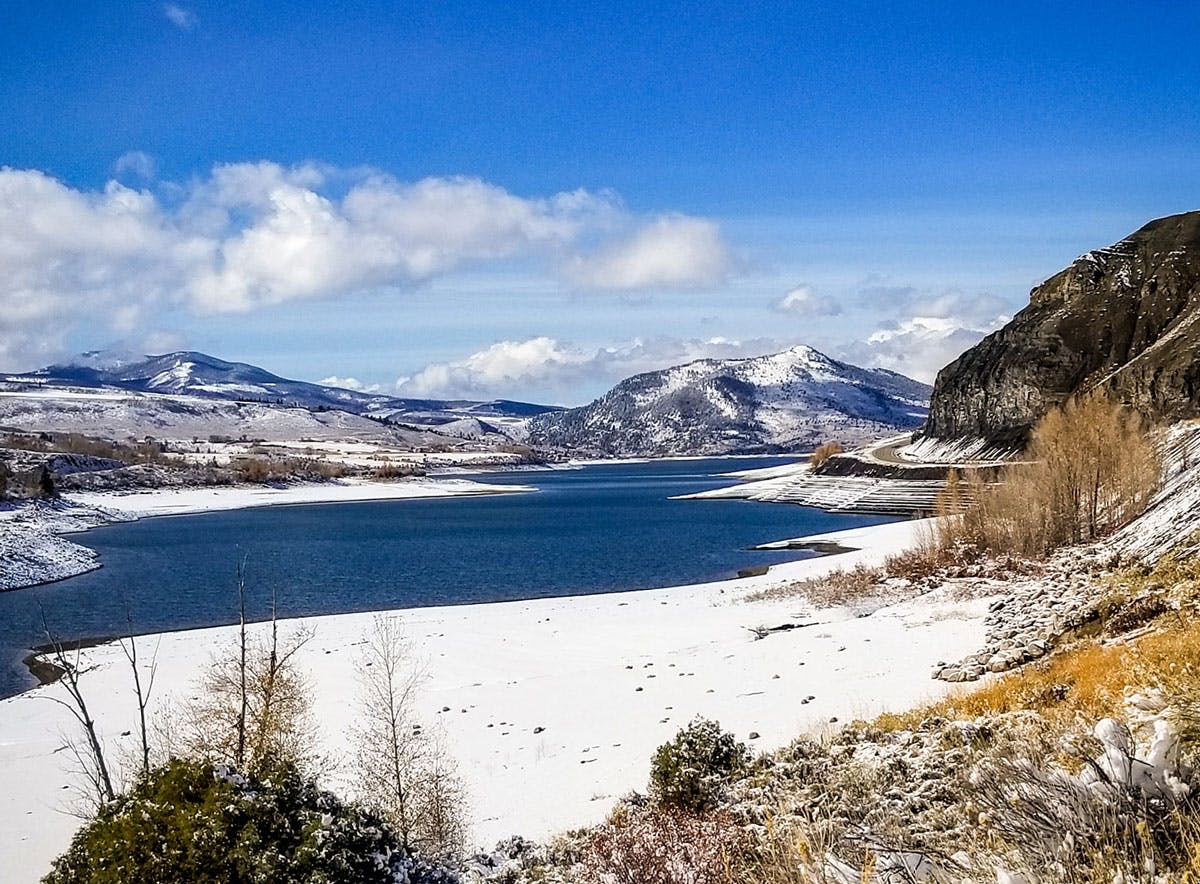 Green Mountain Reservoir near Kremmling is half frozen and covered in snow with mountains and a bright-blue sky with puffy white clouds in the background