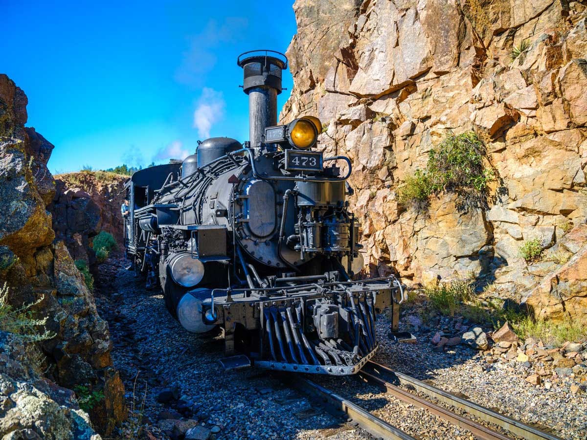 An engine on the Durango & Silverton Narrow Gauge Railroad climbs the rails between two rocky canyon walls in Colorado.