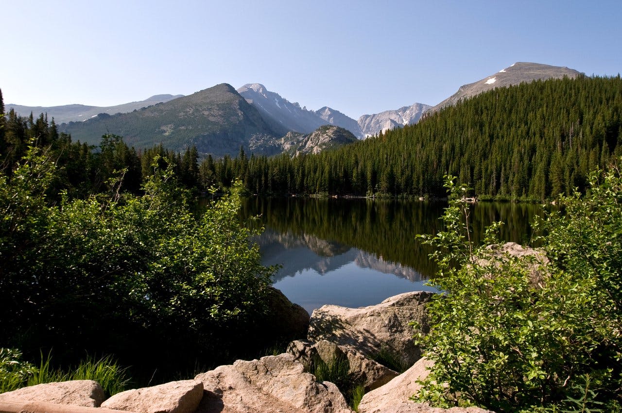 An alpine lake reflects the surrounding peaks on a sunny summer day in Rocky Mountain National Park in Colorado.