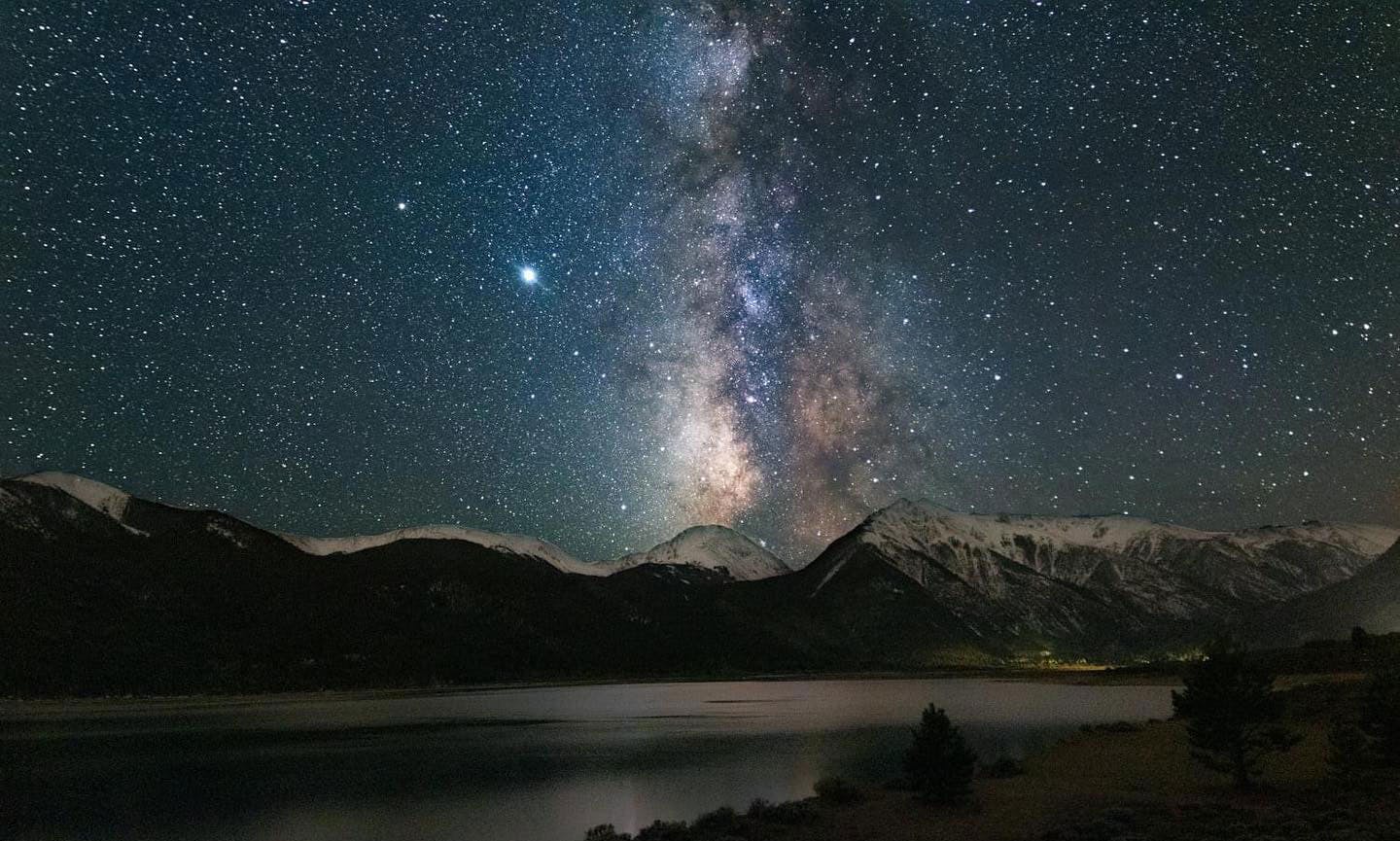 The Milky Way slashes through the night sky and reflects in the surfaces of Twin Lakes in Colorado