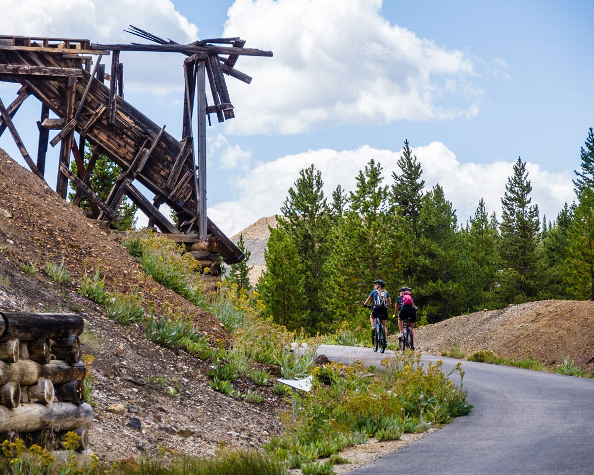 Two people bike a paved trail that passes old mining artifacts on the Mineral Belt Trail in Leadville, Colorado