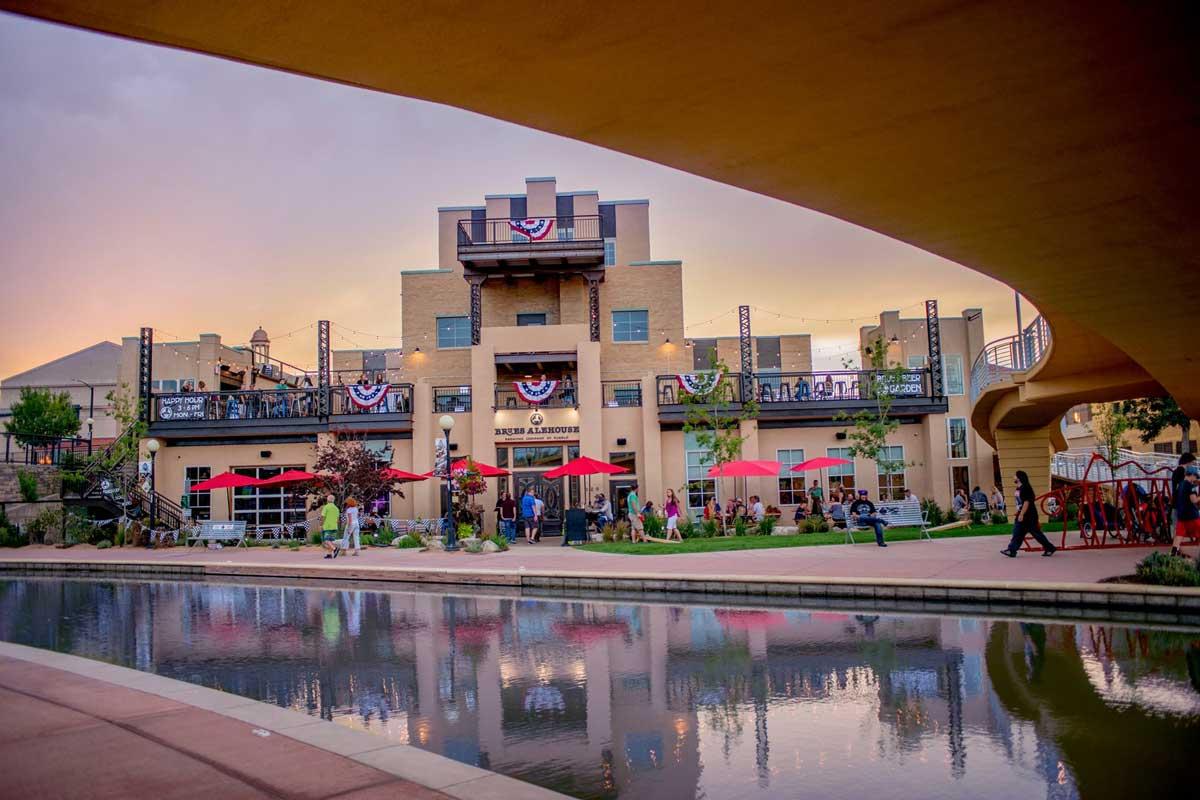 A sunset view of the exterior Pueblo's Brues Alehouse alongside the Historic Arkansas Riverwalk, with red umbrellas covering the outside tables