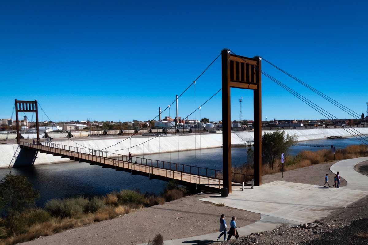 A steel walking bride spans the water of the concrete Pueblo Levee