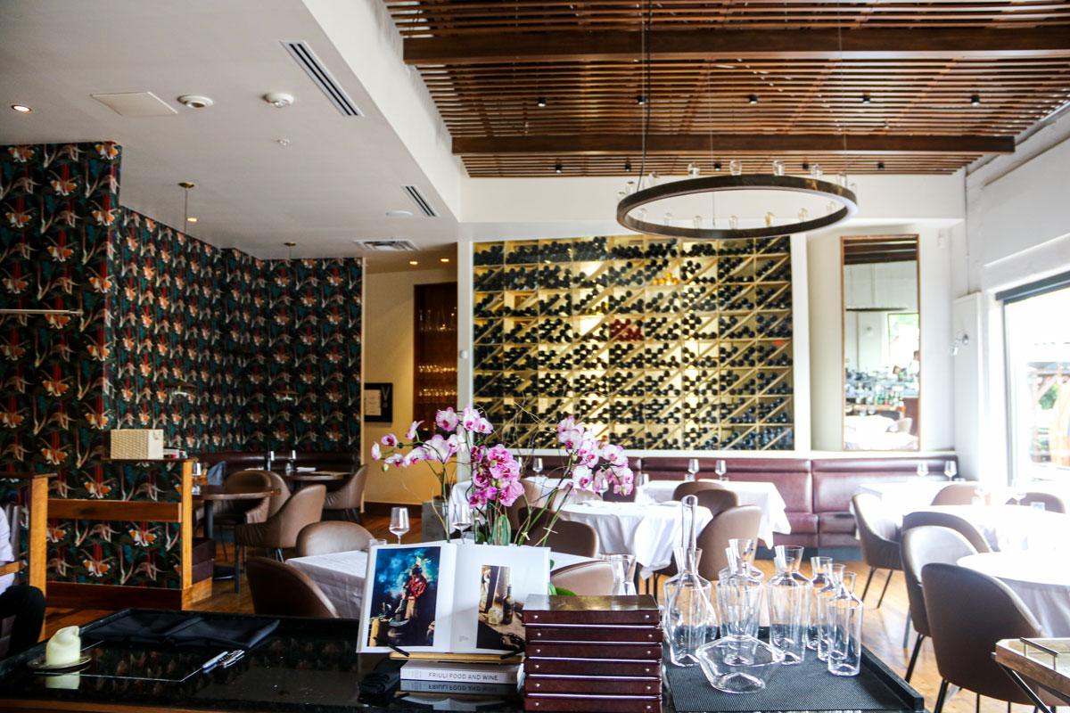 A view into the empty dining room of Frasca, with dark, flowered wallpaper, white-tableclothed tables, a vase of pink orchids