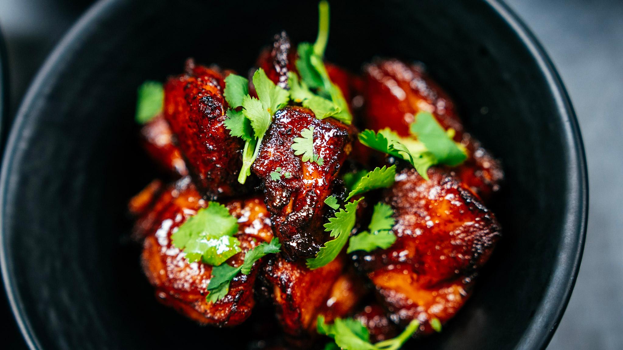 A black bowl holds a reddish dish of spicy pork topped by bright green cilantro