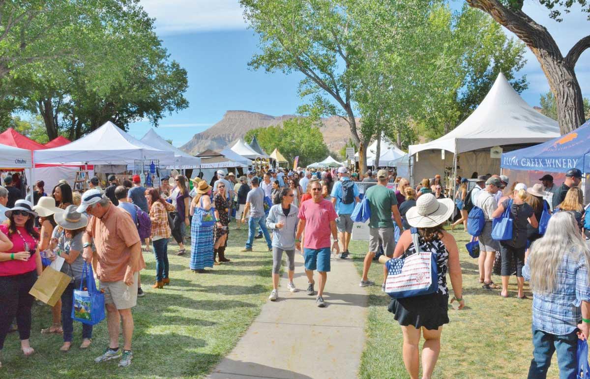 Under the watchful eye of Mt. Garfield, festival goers roam between vendors' white tents which are spread in a tree-line park in Palisade, Colorado.