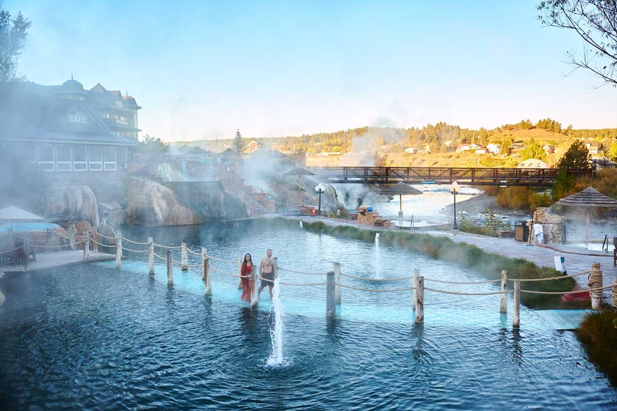 Two people walk on a bridge through steamy pools