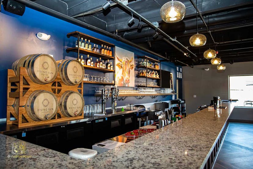 A bar at a distillery is lined with glasses and barrels with spigots