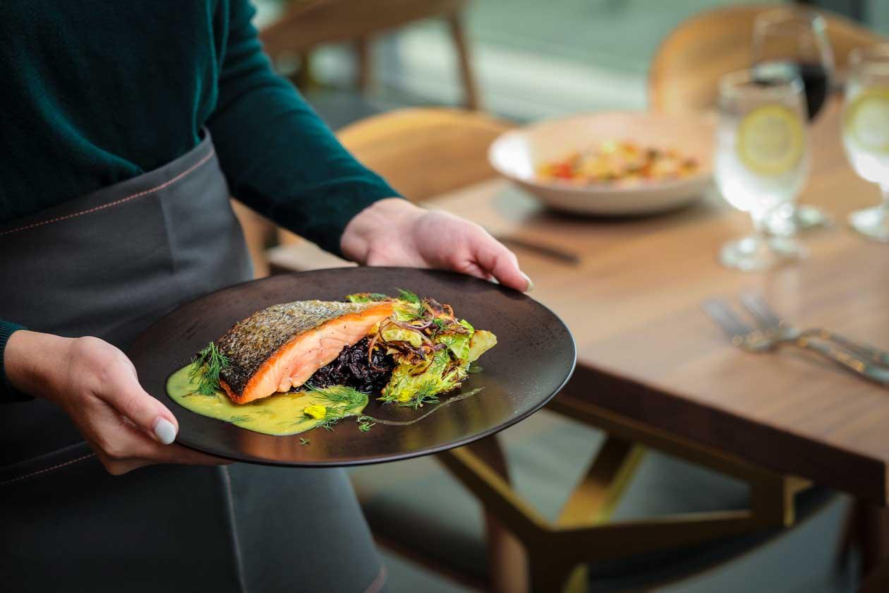 A waitor carries a plate of salmon to a table