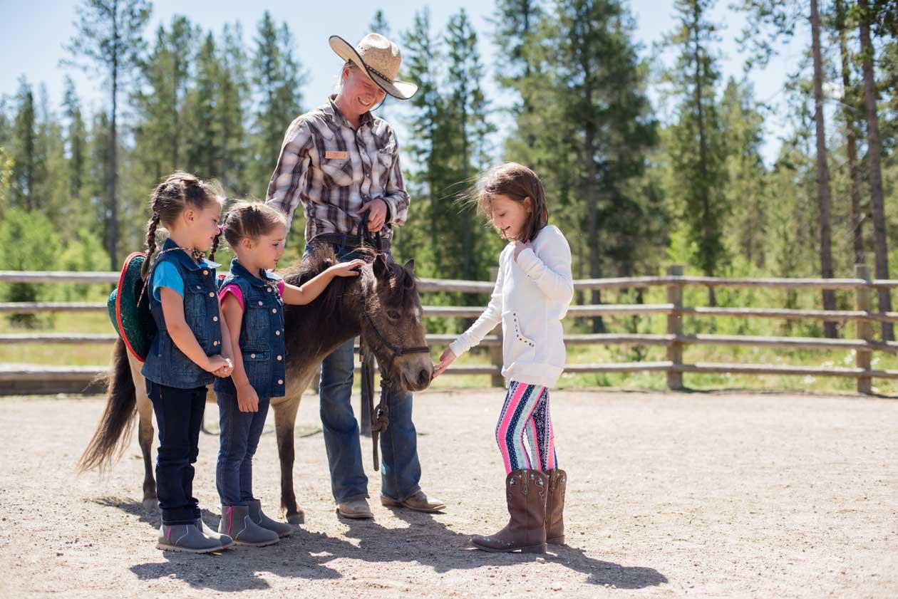 Three girls pet a little horse led by a wrangler