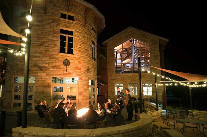 A patio at a brewery at night with white lights strung over the patrons