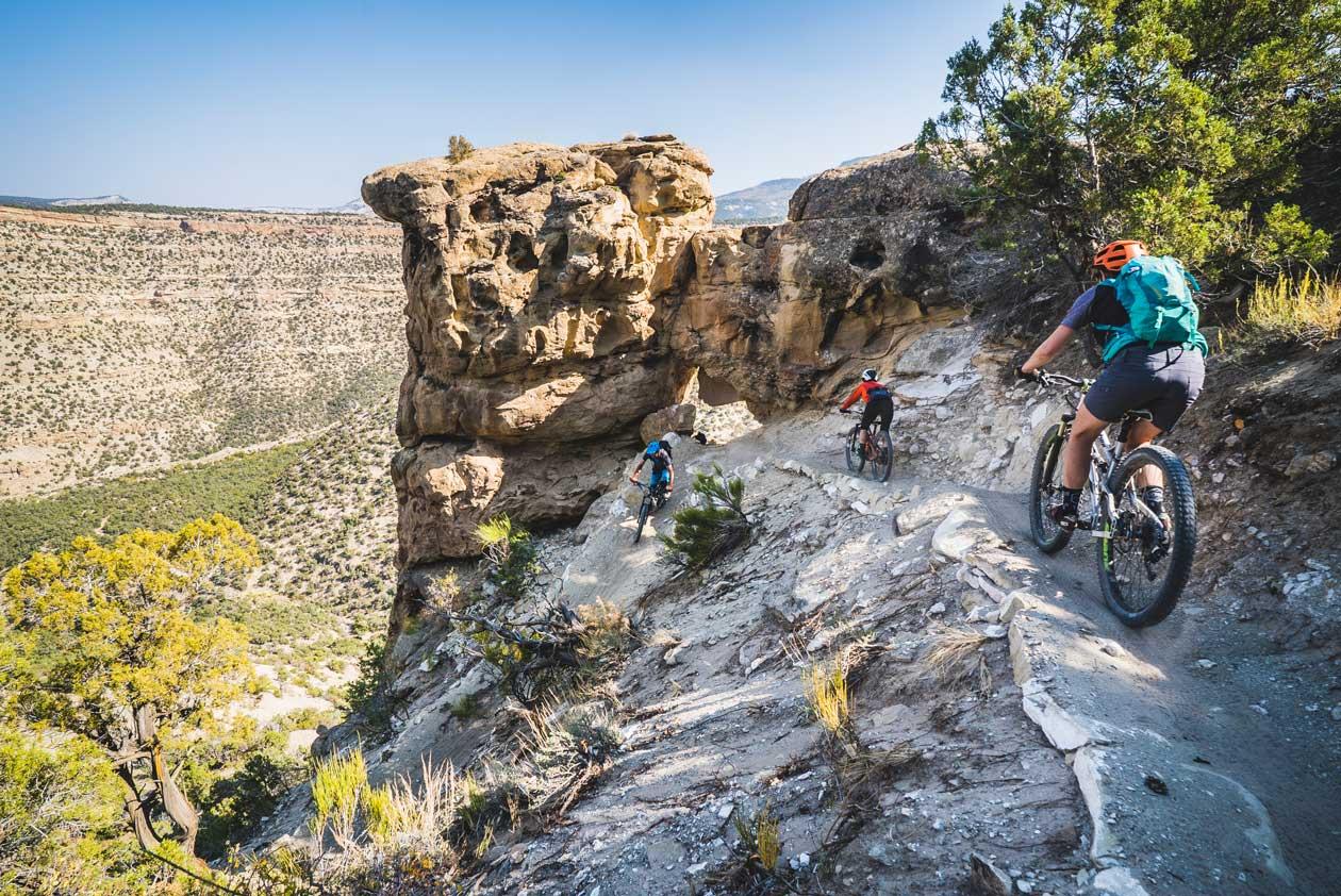 Mountain bikers ride along a ridge toward a canyon