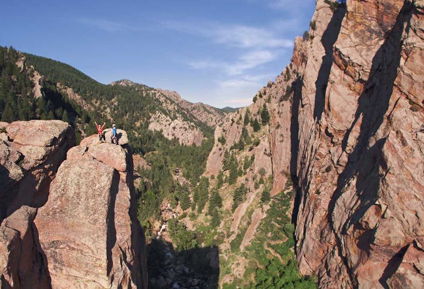 Two people who just climbed to a rocky summit raise their arms in celebration