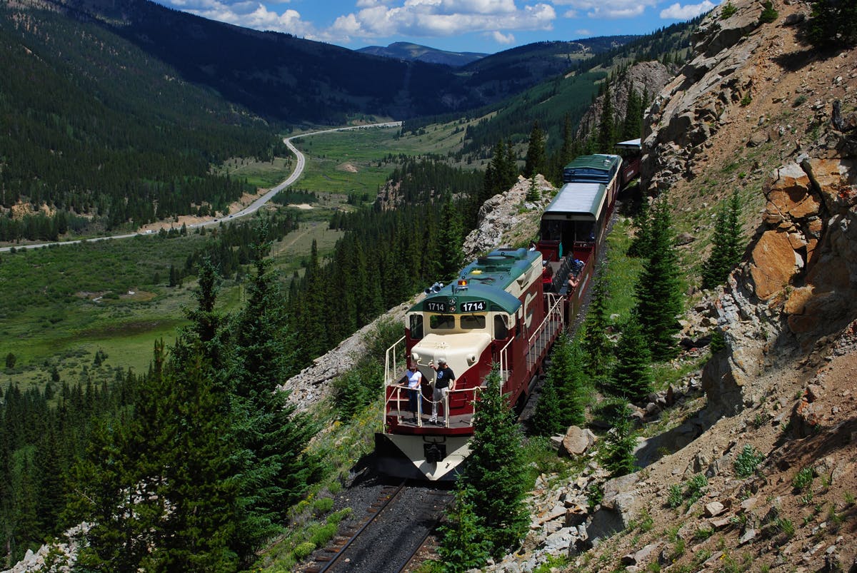 An aerial view of the Leadville Railroad train snaking through the lush green foliage of the mountains