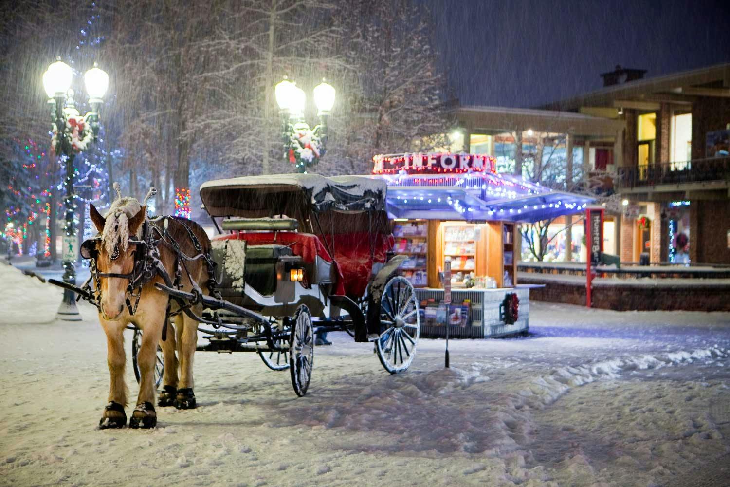 A horse-drawn carriage makes it's way through a snowy Aspen with an information booth in the background.