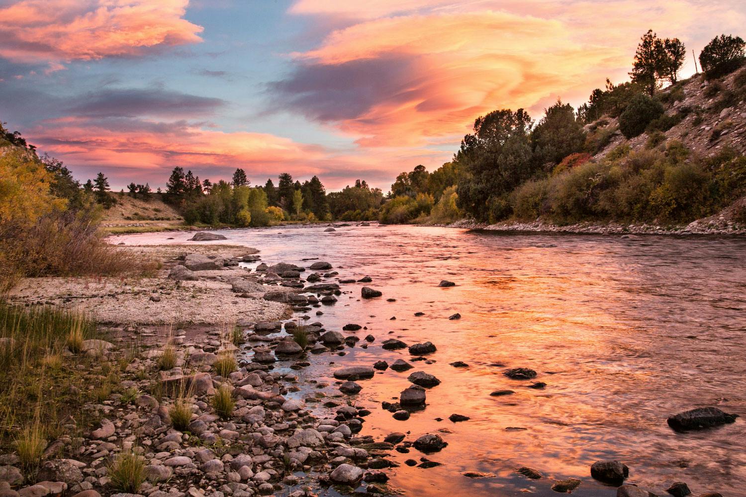 The setting sun turns the clouds pink, which are reflected in the river's tranquil waters at Browns Canyon National Monument in Colorado.