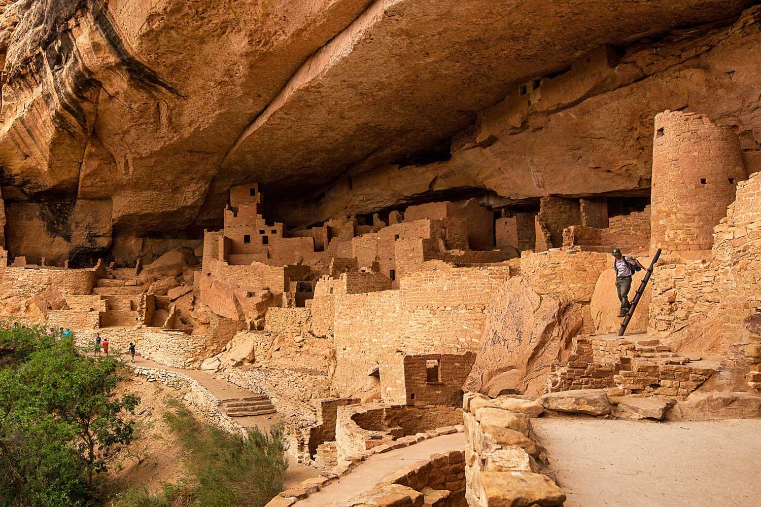 A visitor climbs down a short ladder after exploring an areas of the cliff dwellings at Mesa Verde National Park.