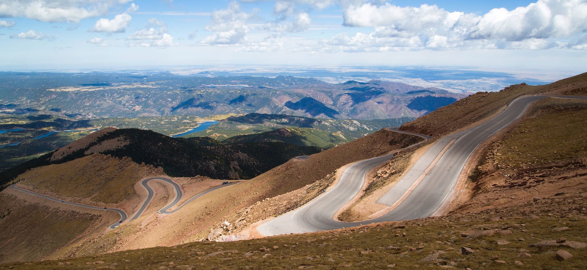 A winding road on a mountain overlooks a large valley spreading out in the distance