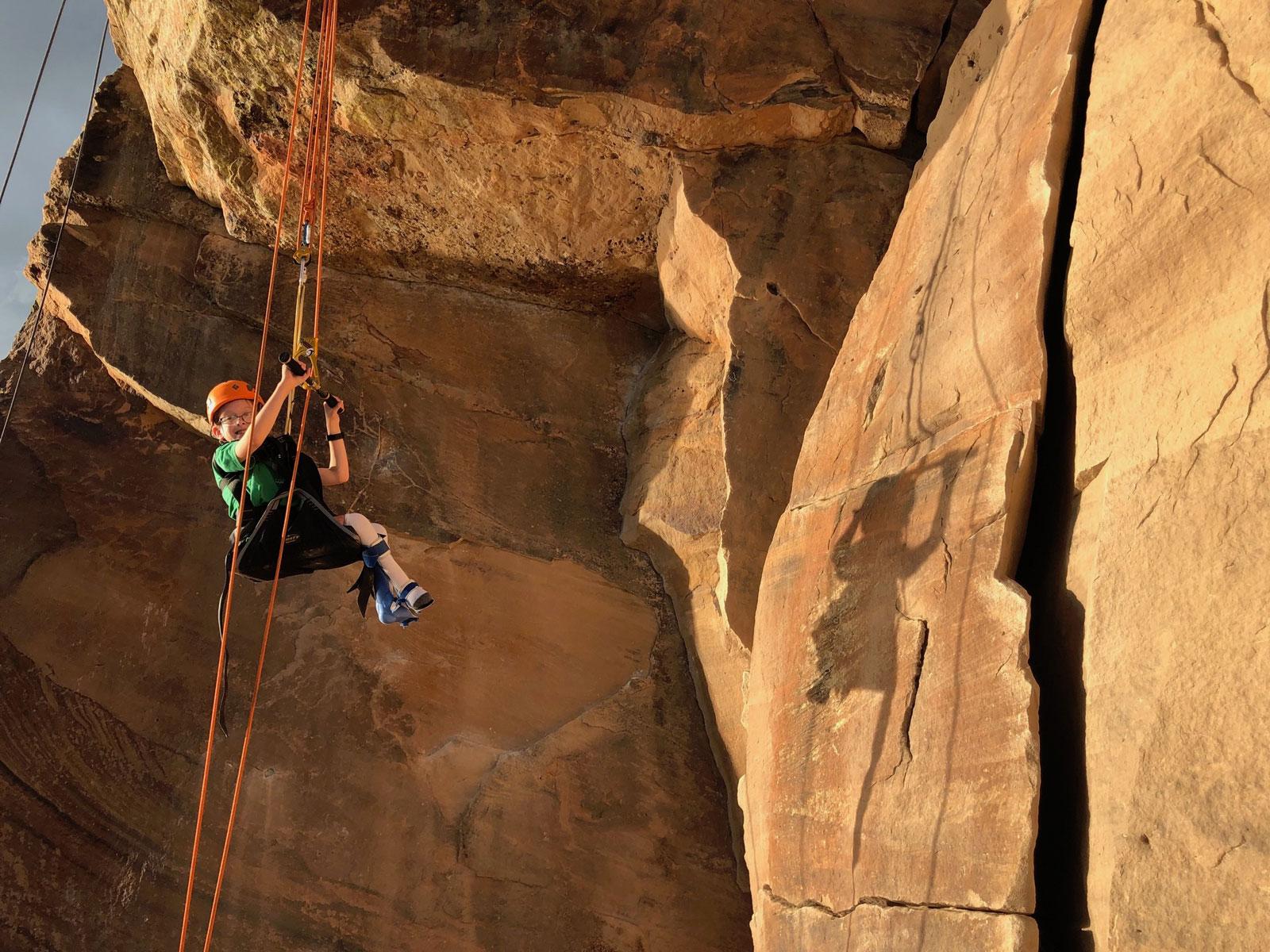 A child climbs a tan rock face at Horsetooth Reservoir using adaptive equipment near Fort Collins, Colorado.