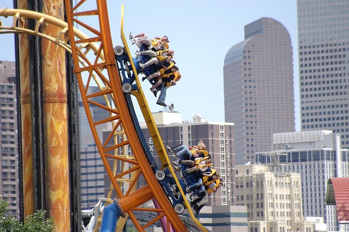 People riding a yellow rollercoaster head skyward with a couple of Denver's skyscrapers in the background