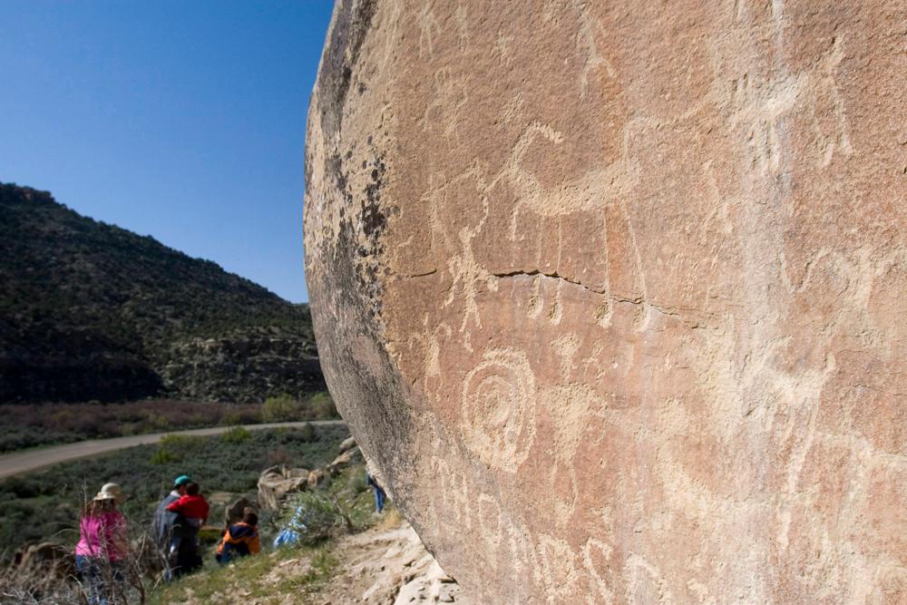 A tour group gazes up, where pictographs are carved into a rock face