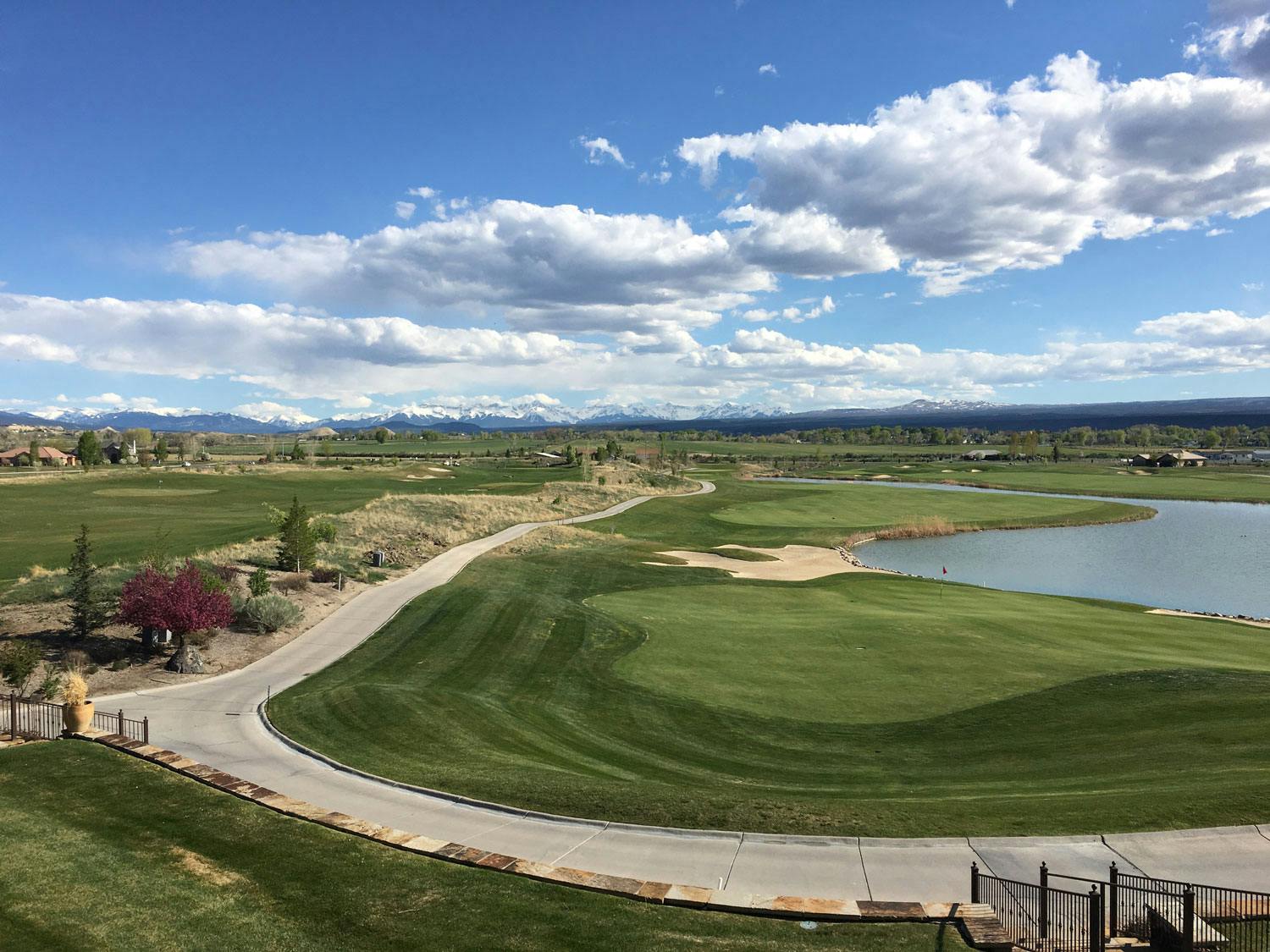 A Kelly-green golf course sits under a bright-blue sky with white clouds with mountains in the far distance.