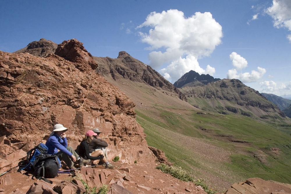 Two backpackers rest on a red-rock trail that leads to the summit of peak